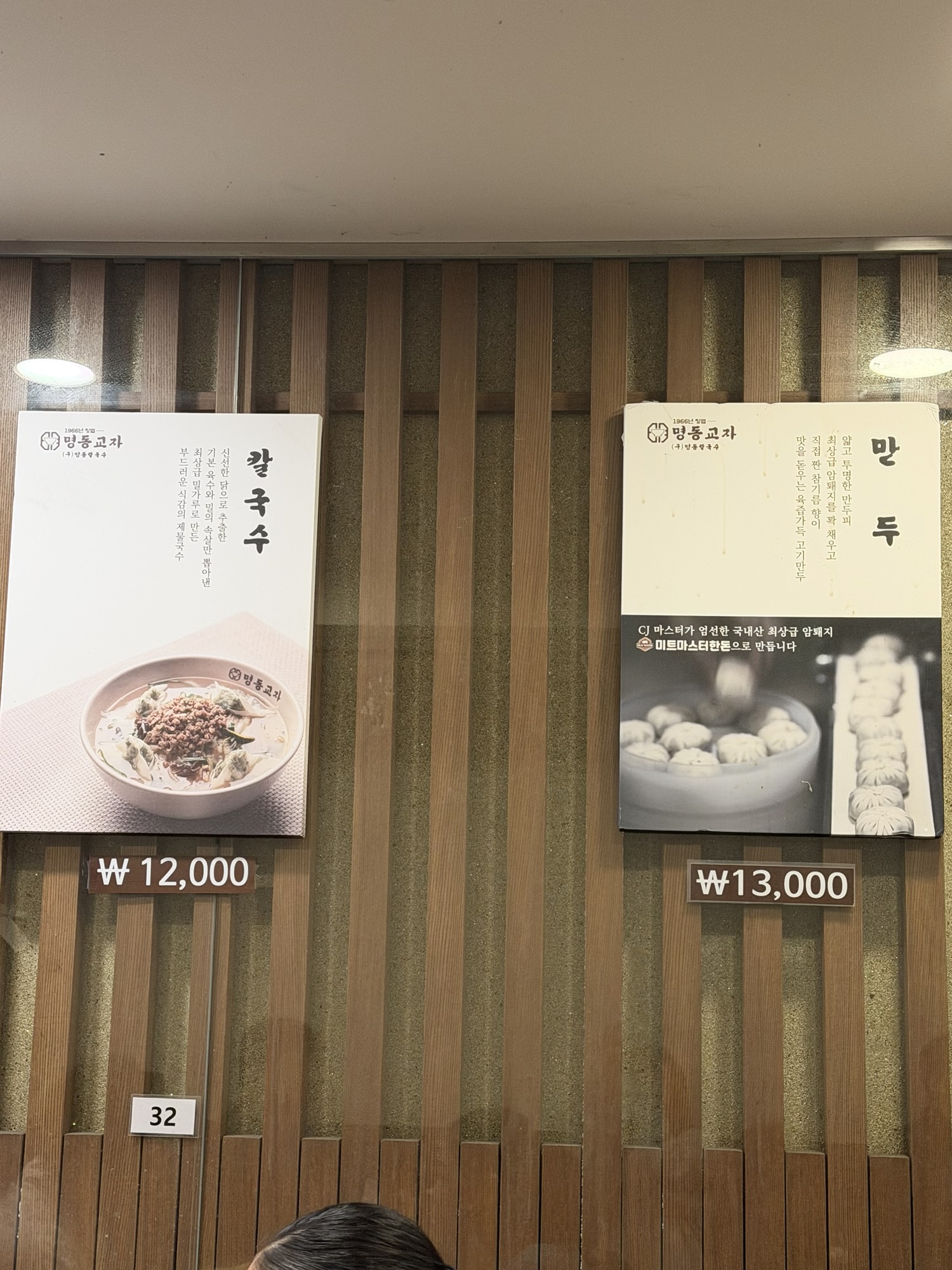 Myeongdong Kyoja menu board showing kalguksu at 12,000 won and mandu at 13,000 won