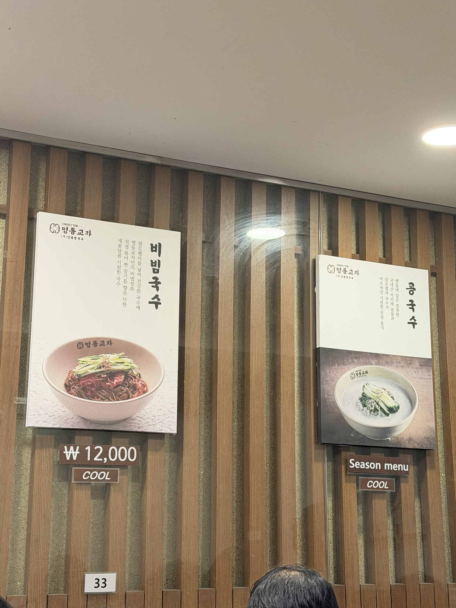 Myeongdong Kyoja menu board showing bibim-guksu at 12,000 won and seasonal kongguksu