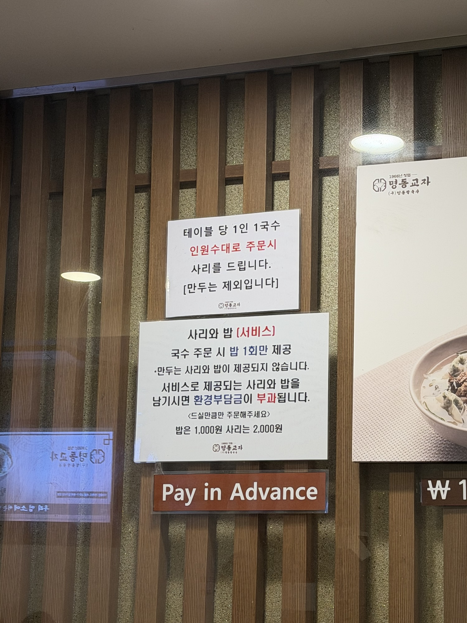 House rules sign at Myeongdong Kyoja explaining free sari and rice add-ons with noodle orders