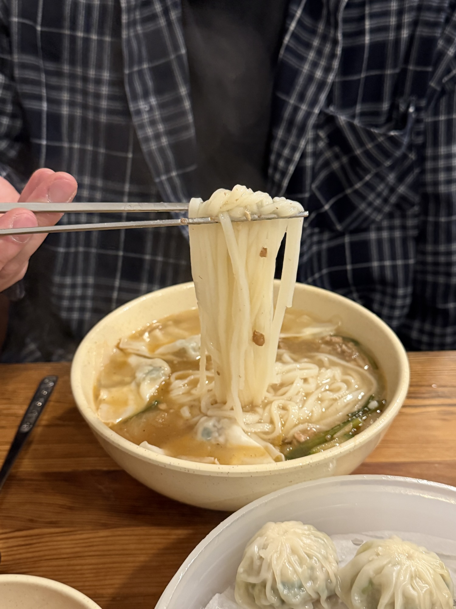 Hand-cut wheat noodles being lifted from the kalguksu bowl at Myeongdong Kyoja