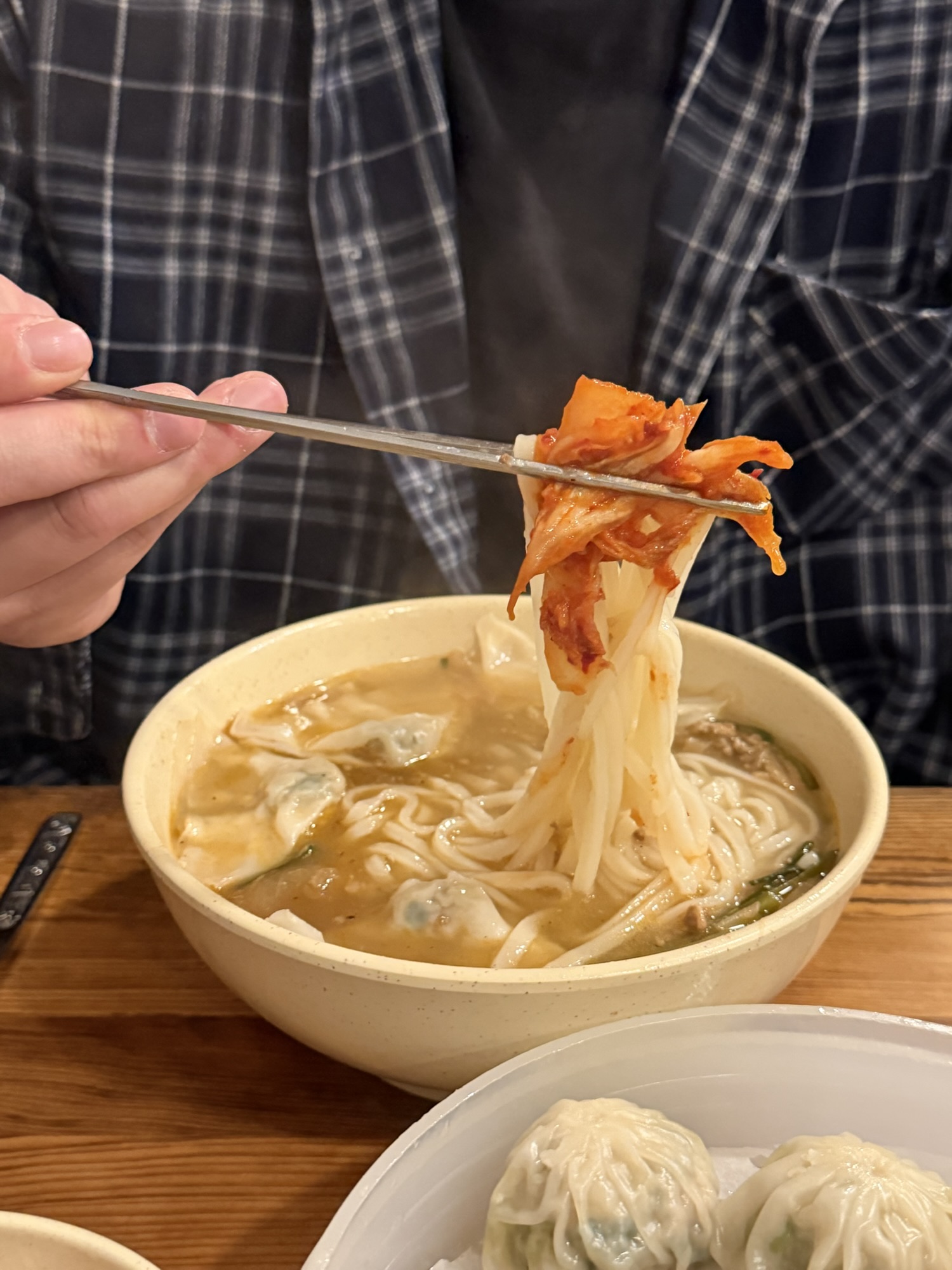 Chopsticks lifting kalguksu noodles topped with garlic kimchi at Myeongdong Kyoja