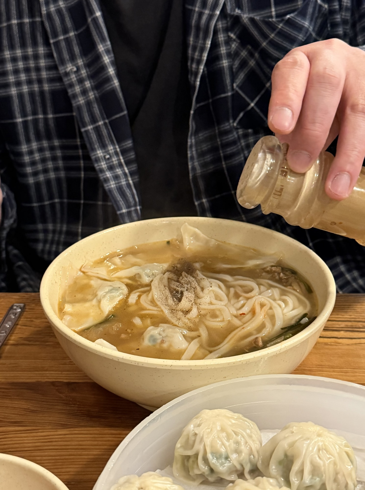 Hand sprinkling white pepper into a kalguksu bowl at Myeongdong Kyoja
