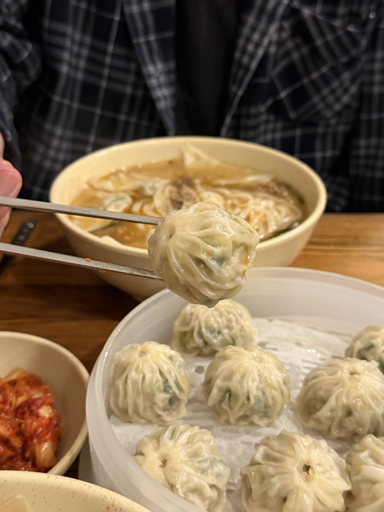 Single steamed mandu held by chopsticks above a plate of ten Myeongdong Kyoja dumplings