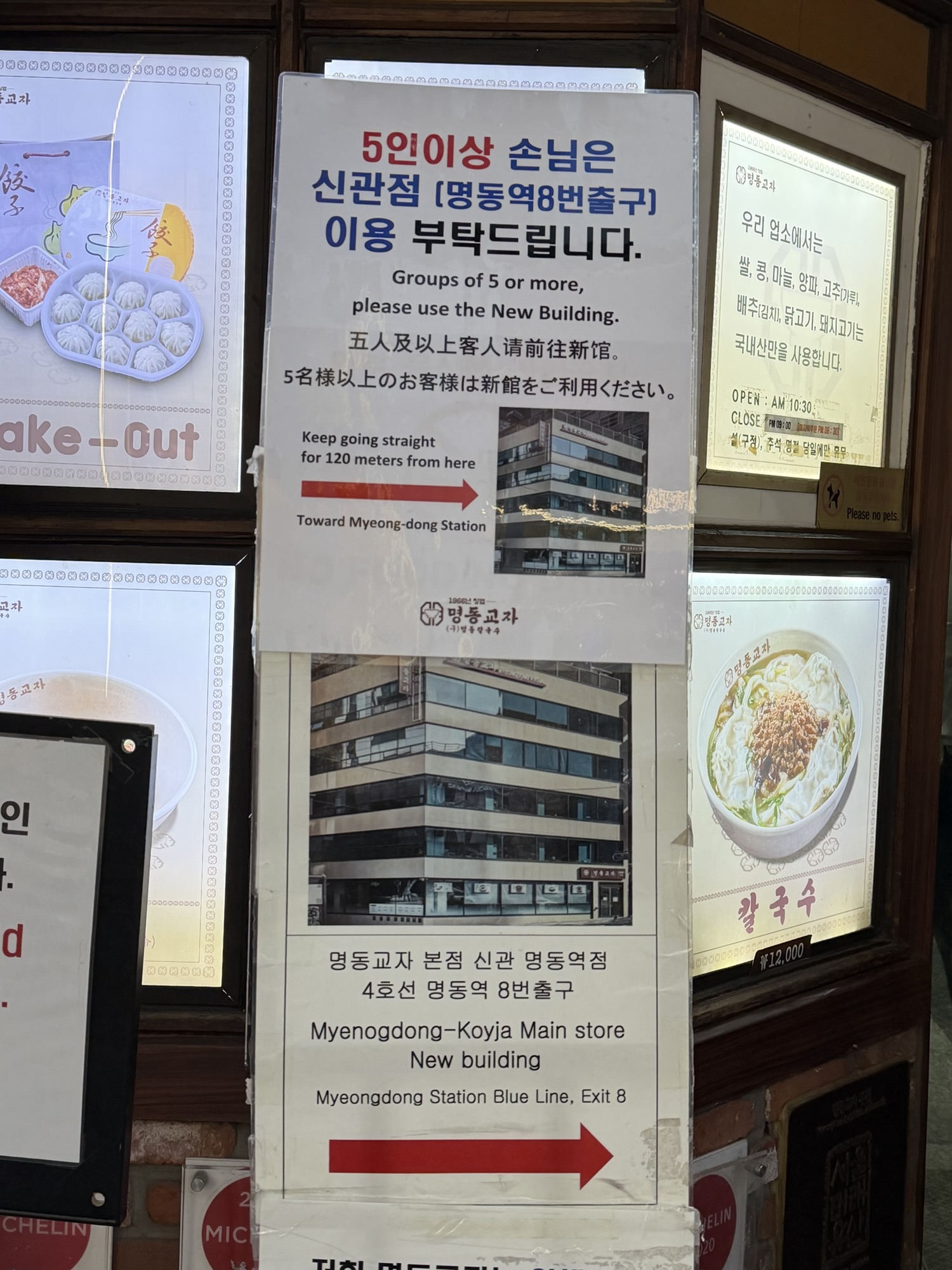 Sign directing groups of 5 or more to the Annex branch of Myeongdong Kyoja, 120 meters toward Myeongdong Station Exit 8