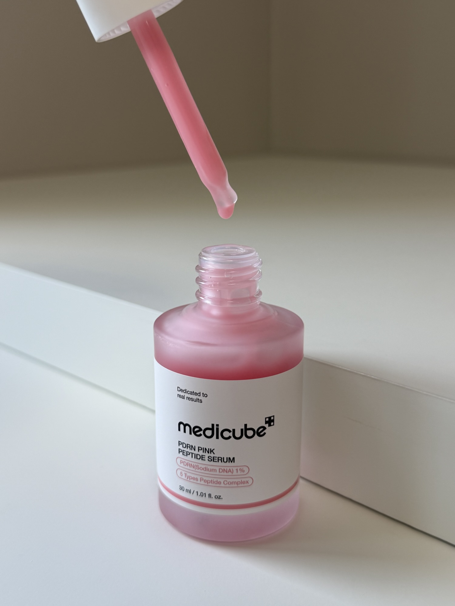 Close-up of Medicube PDRN Pink Peptide Serum dropper showing the silicone teat and watery serum dripping back into the bottle