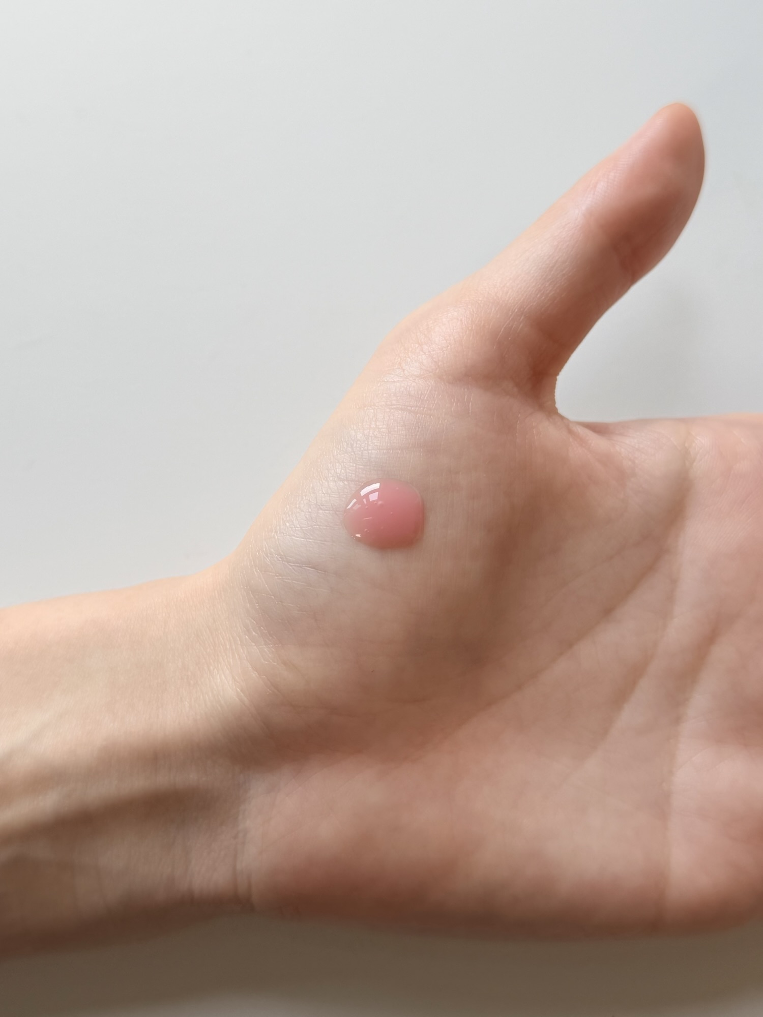 Single drop of Medicube PDRN Pink Peptide Serum on the back of a hand showing the small pink bead before spreading