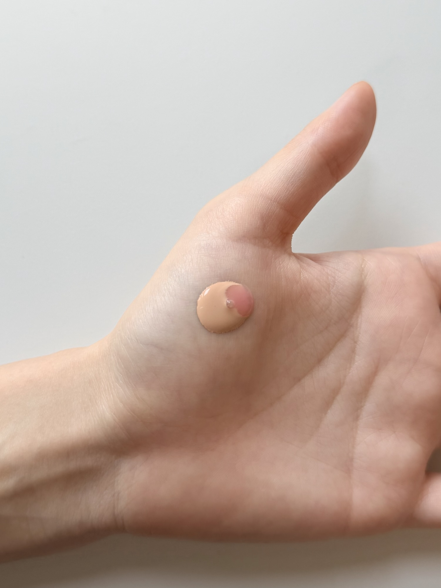 A drop of Medicube PDRN Pink Peptide Serum mixed into a drop of foundation on the back of a hand before blending