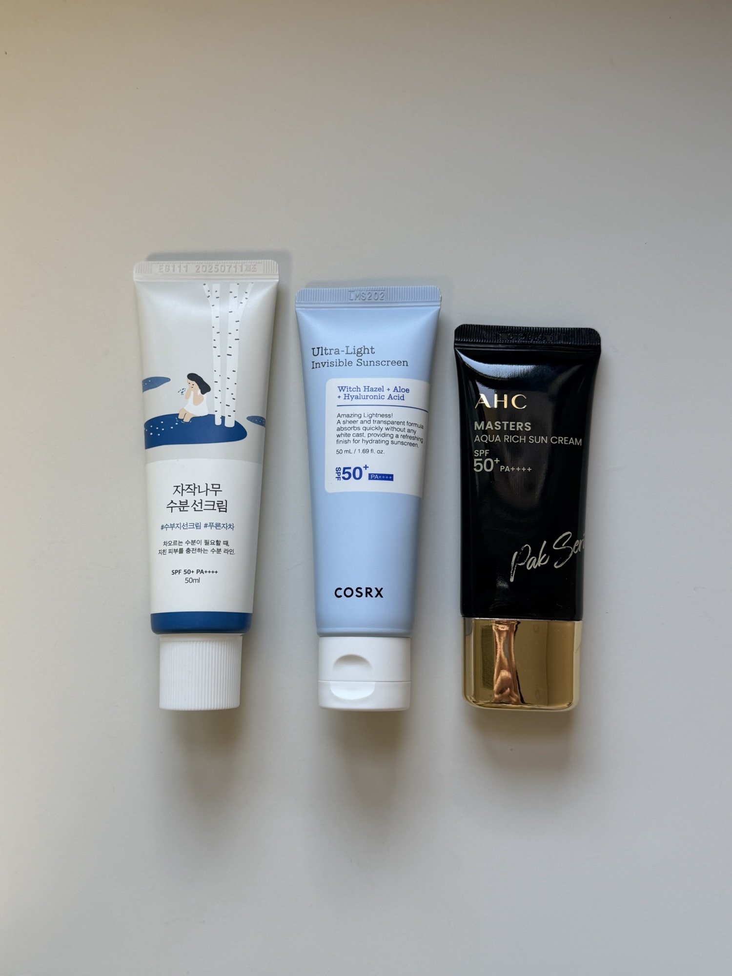 ROUND LAB, COSRX, and AHC moisture sunscreens lined up on a desk
