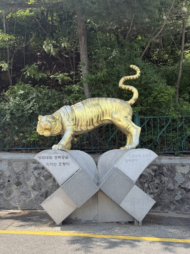 Street-level view near the Inwangsan tiger statue trailhead, pedestrians and parked cars along the road