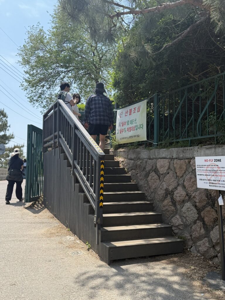 Inwangsan trail entrance — metal steps with safety gate and Korean warning sign, hikers entering
