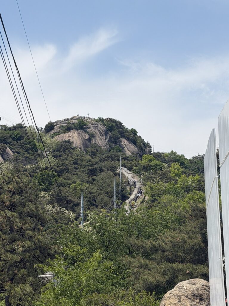 First rocky peak of Inwangsan visible from the trail — looks like the summit but is not, stone steps winding up the exposed granite