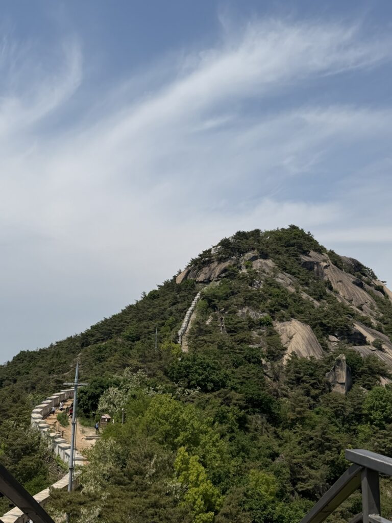 View of Inwangsan's true summit rocky peak from the intermediate ridge, with stone steps visible on the approach