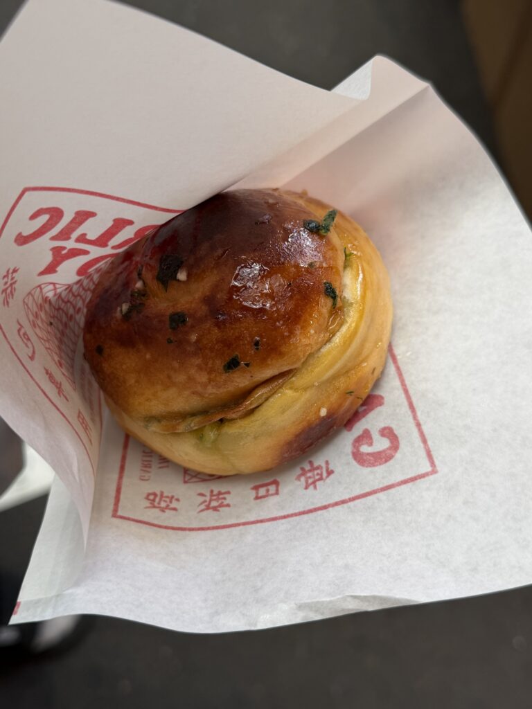Garlic Boy's basic garlic bread — a fist-sized glossy bun topped with garlic and parsley, on the shop's printed paper wrapper