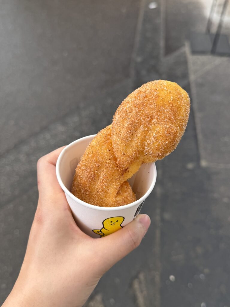 Two glutinous rice twisted donuts dusted with sugar and cinnamon, in a paper cup with the shop's yellow mascot