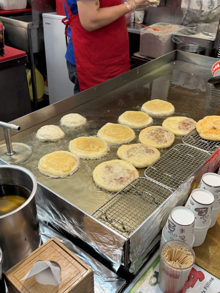 Hotteok (Korean sweet pancakes) frying on a large griddle at a Gwangjang Market stall, golden-brown crusts pressed flat
