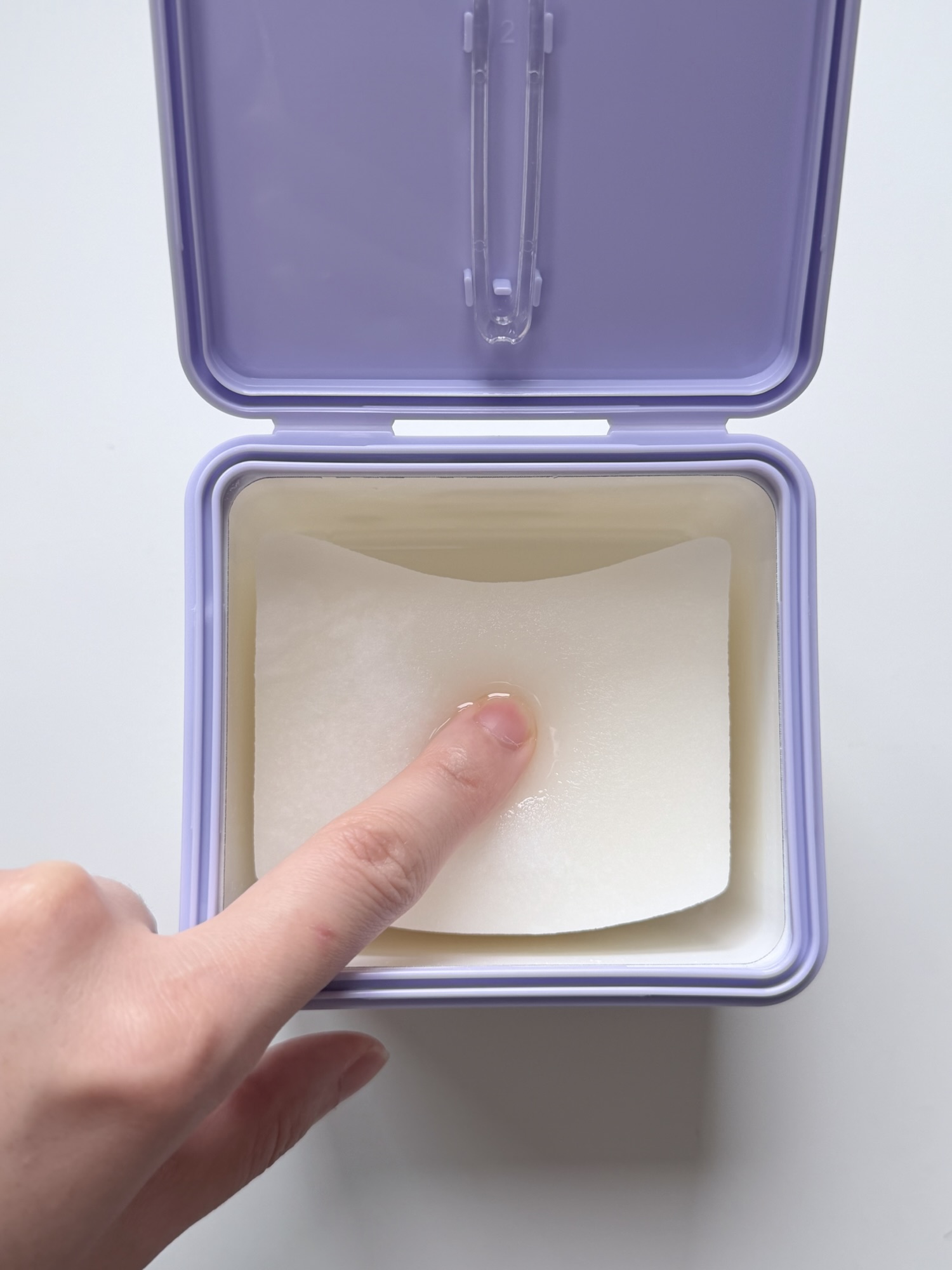 Lightly pressing a Rejuran toner pad to show essence welling up — fully saturated pads
