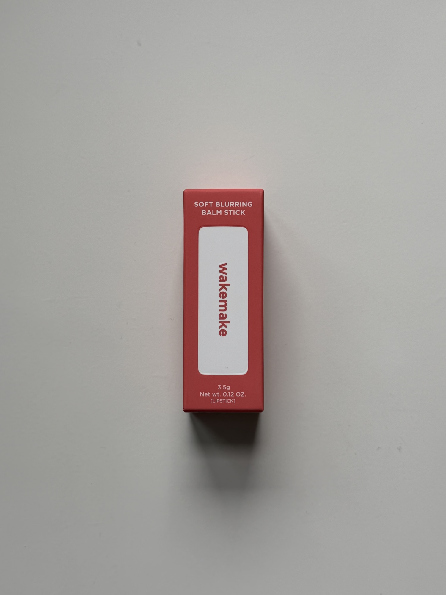 Wakemake Soft Blurring Balm Stick outer box — minimalist coral-red packaging, 3.5g