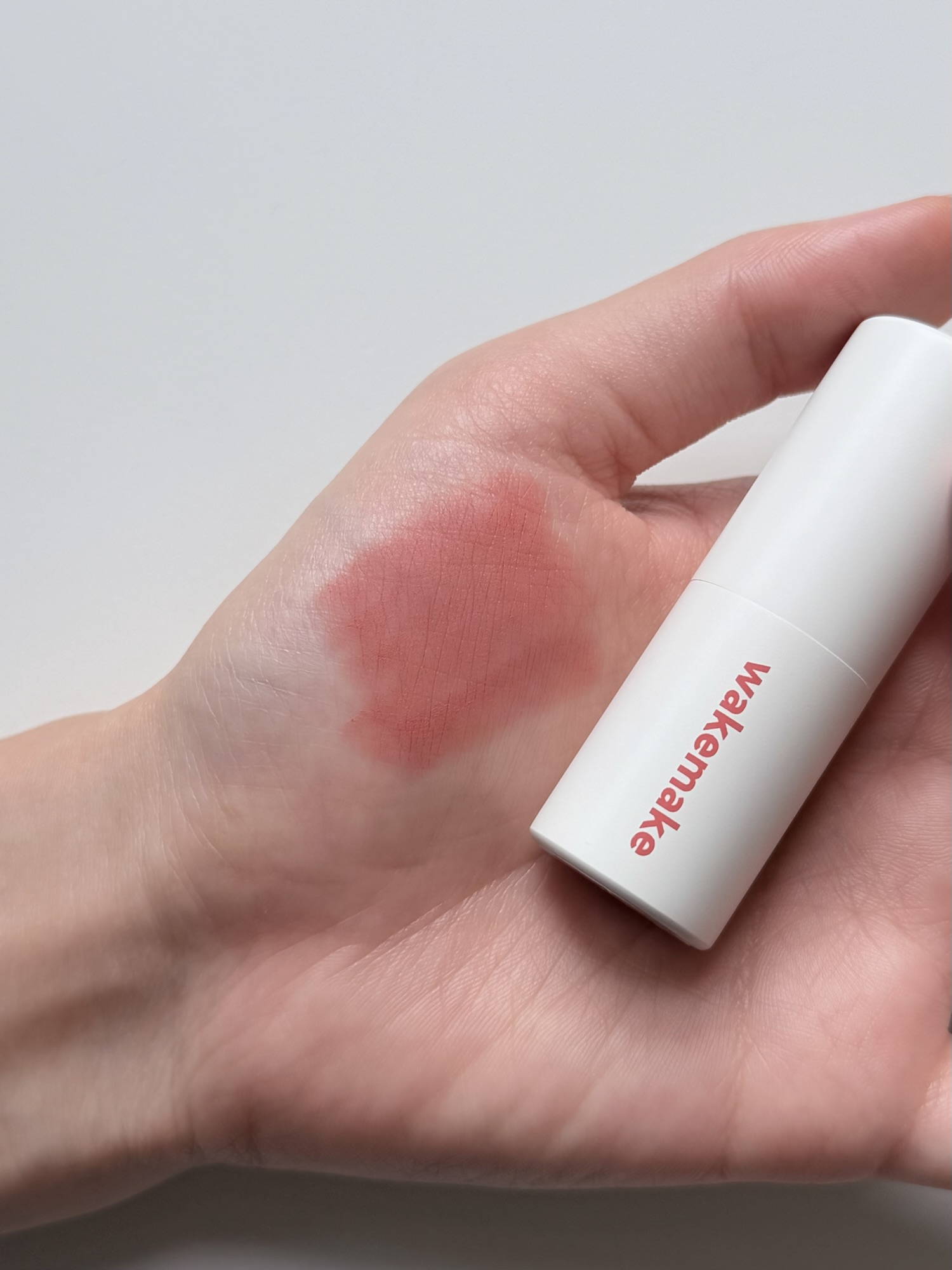Wakemake Blurring Balm Stick #08 swatched on hand — one layer: sheer dusty coral-pink, smooth application