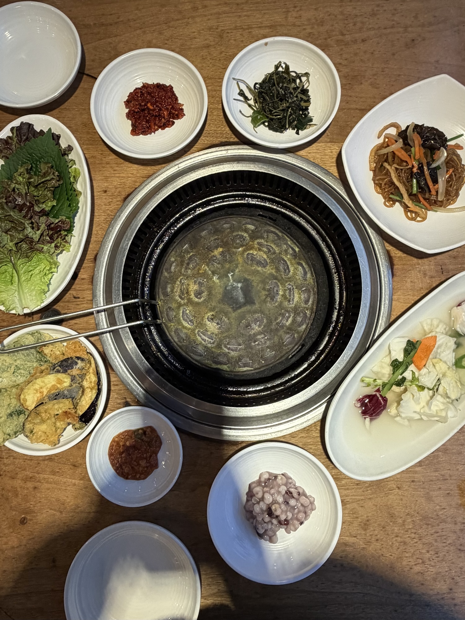 The banchan spread at Songdo Galbi — japchae, vegetable tempura, seasoned namul greens, and spicy dried radish strips instead of the usual raw garlic and onions
