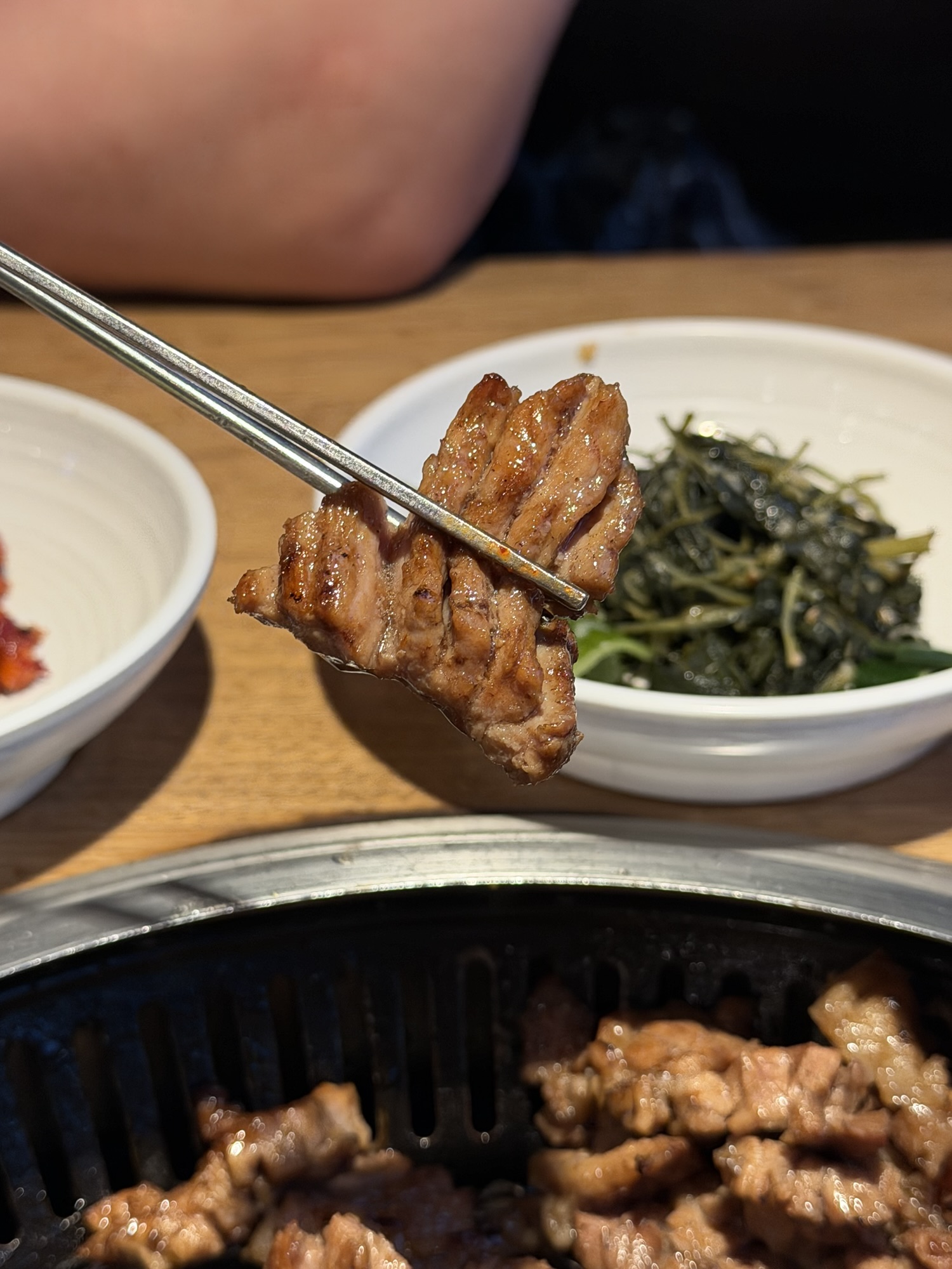 Chopsticks holding a single bite-sized piece of charcoal-grilled pork galbi at Songdo Galbi — caramelized exterior, tender inside
