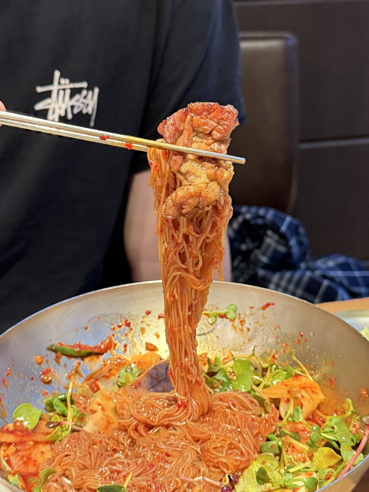 Chopsticks lifting a tangle of spicy naengmyeon noodles with a piece of galbi — the galbi-and-naengmyeon finish at Songdo Galbi