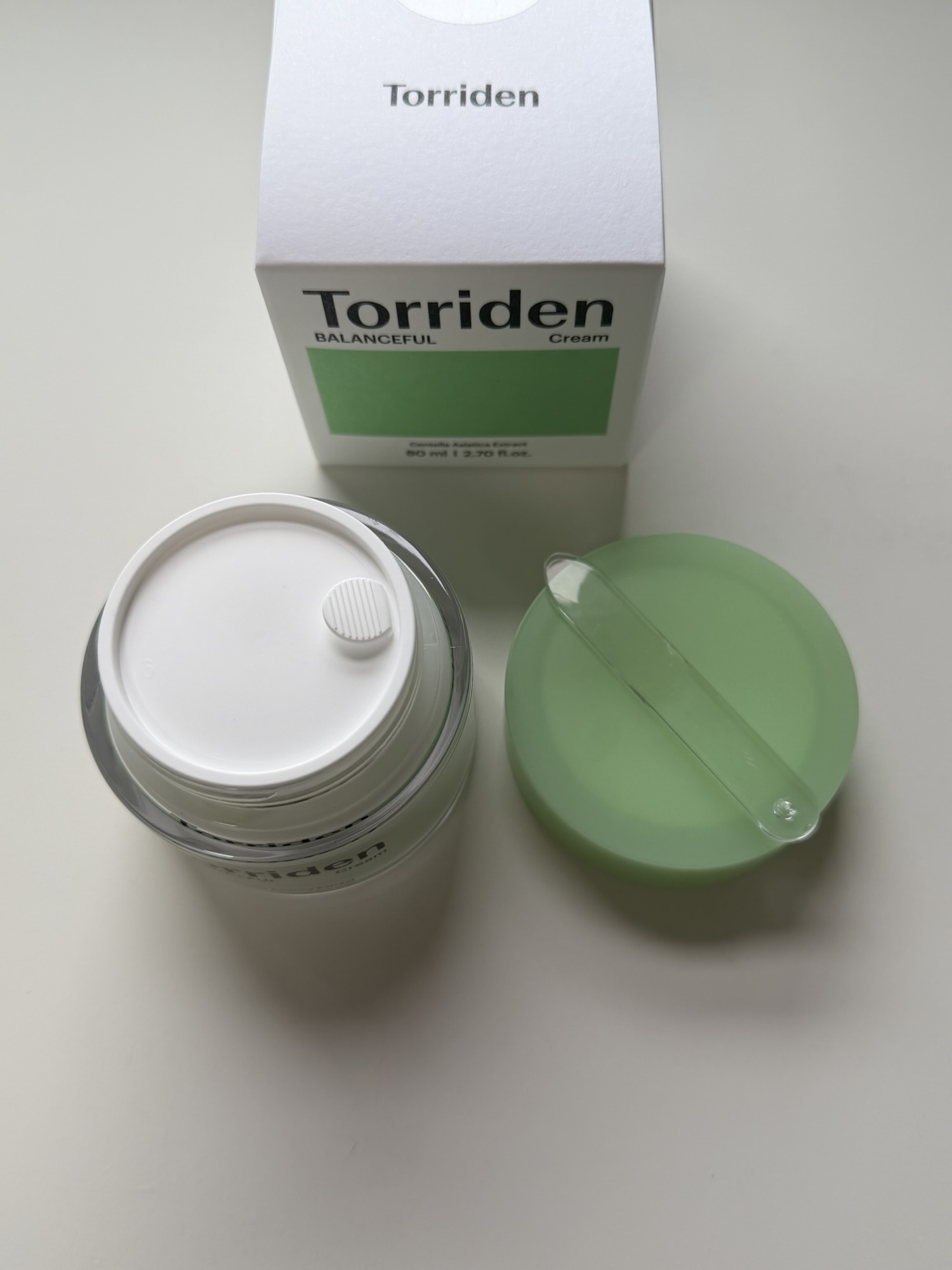 Torriden Balanceful Cica Cream jar opened to show the inner cap and included spatula resting on top of the cream