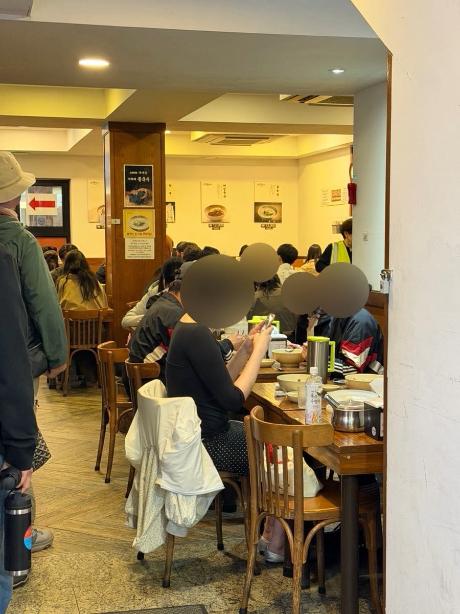 Packed first floor dining room at Myeongdong Kyoja main branch, diners seated tightly at wooden tables