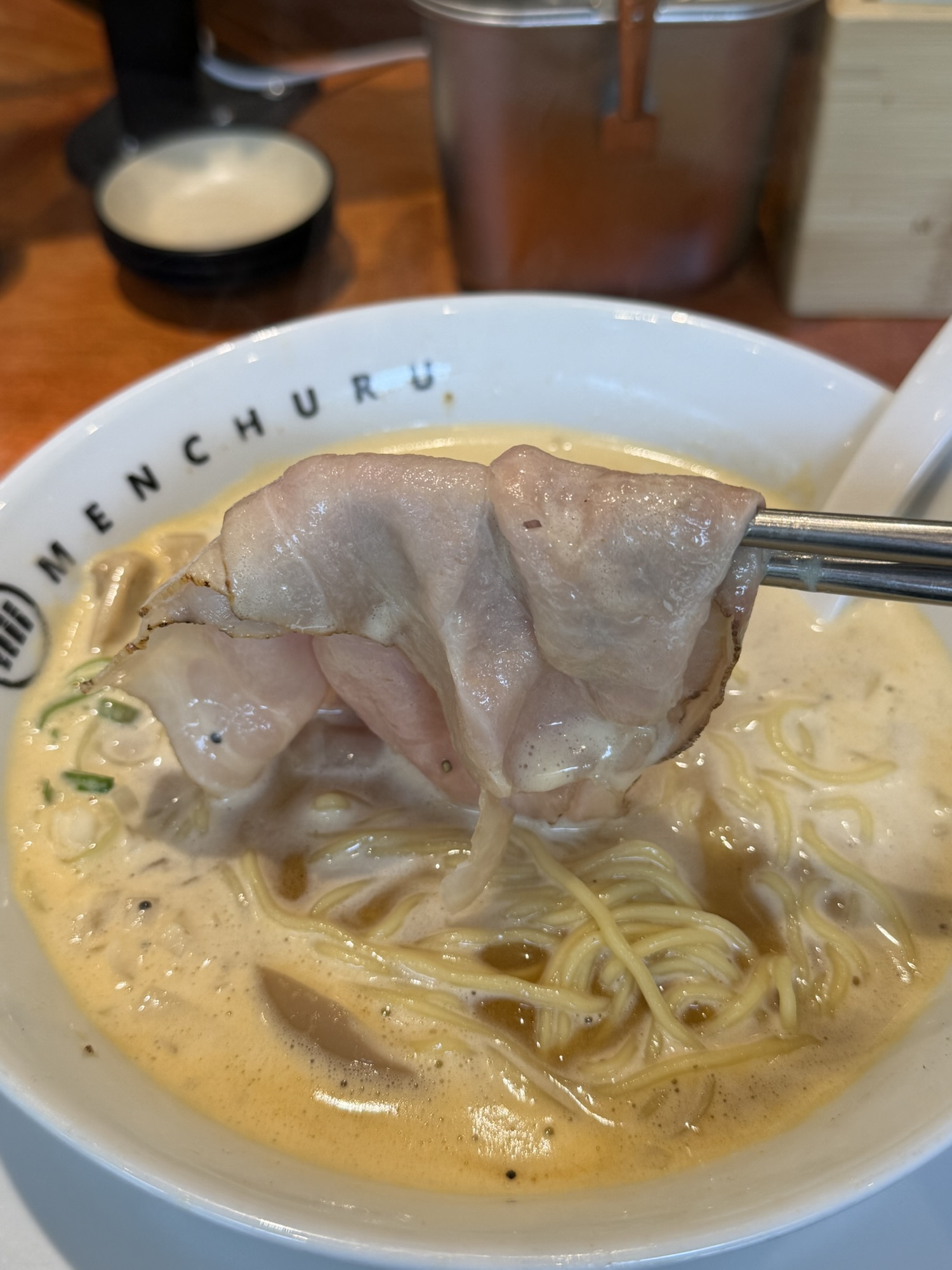 Thin chashu lifted with chopsticks from spicy paitan ramen at Menchuru Yeouido