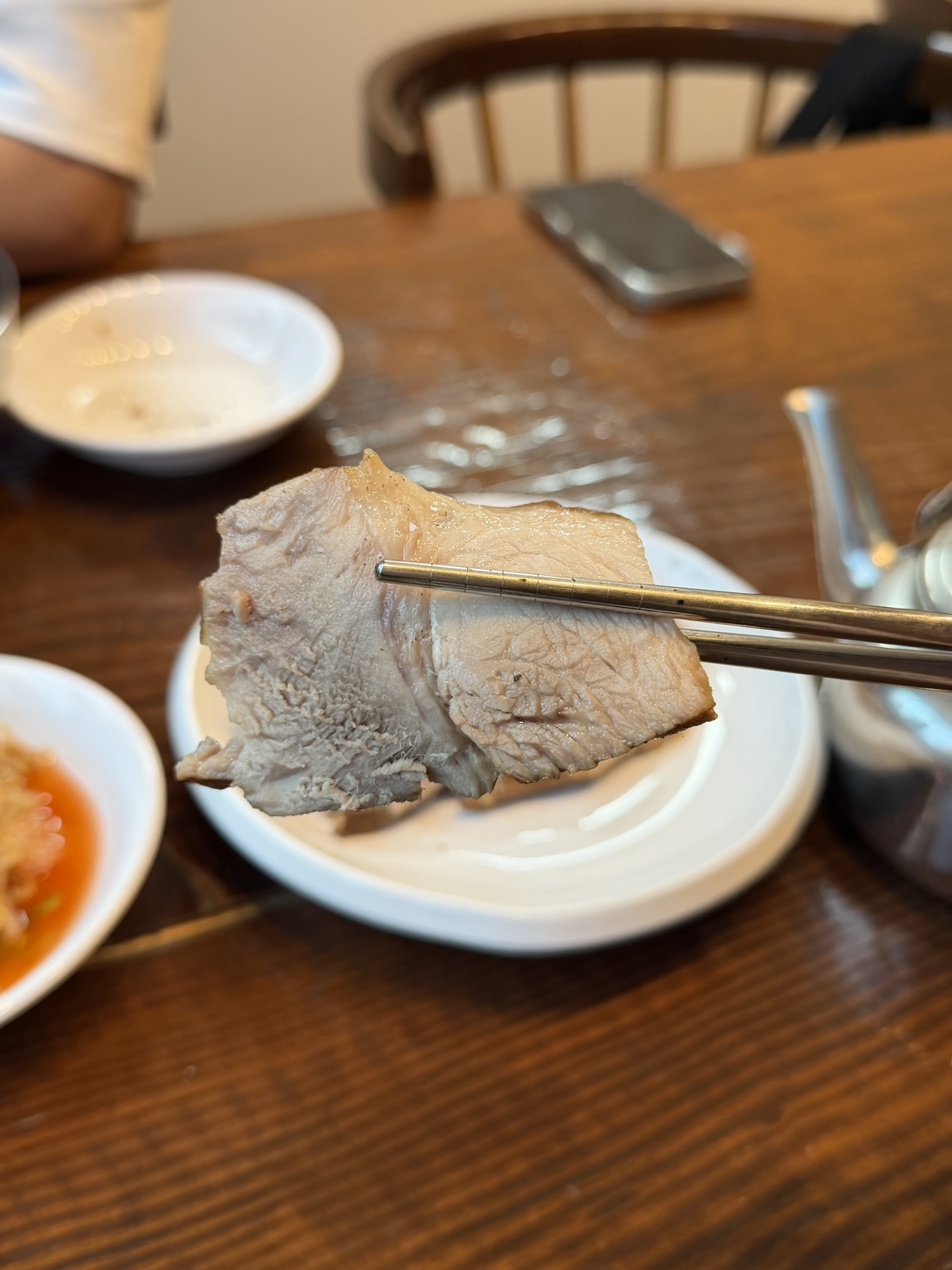 Close-up of suyuk boiled pork slice held with chopsticks
