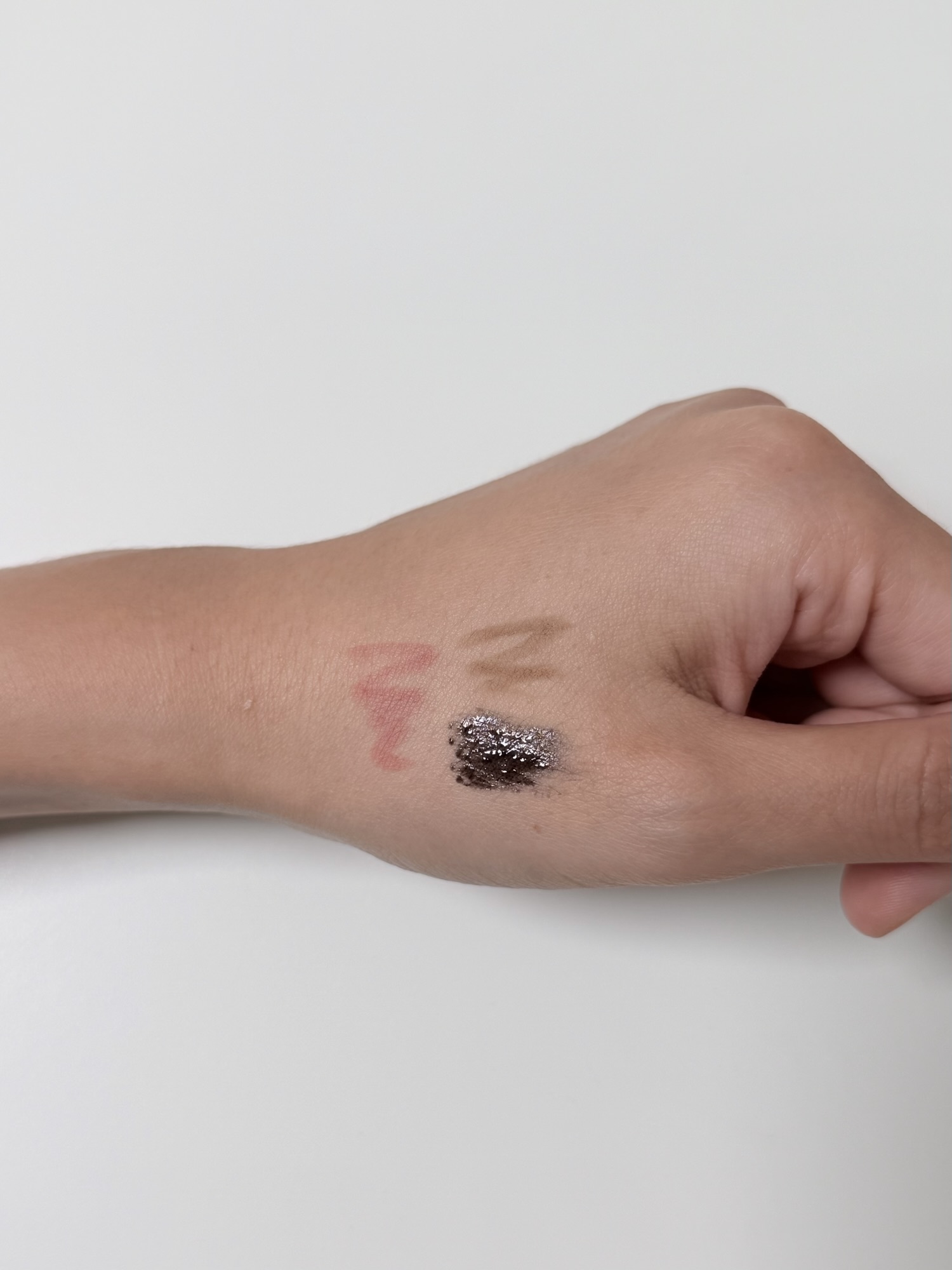 Lip pencil eyebrow pencil and mascara swatches on the back of a hand before cleansing