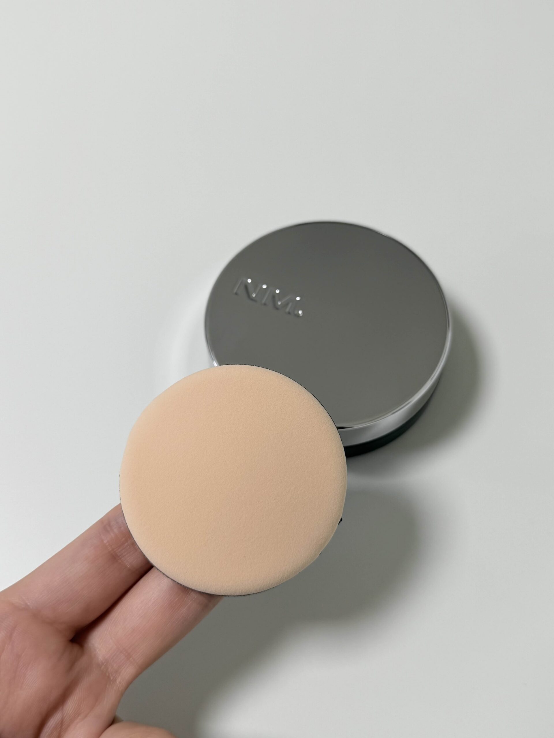 NAMING Layered Fit Cushion puff held in front of the silver compact